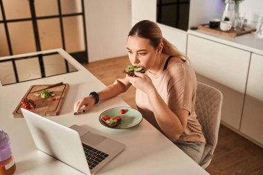 Protez kollu güzel genç bir kadın modern mutfakta yemeğini yiyor.