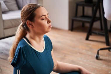 Ampüte eli olan beyaz kadın rahat bir şekilde odasında yerde oturuyor.