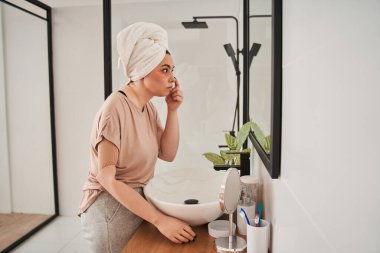 Protez elli beyaz kadın spa ameliyatı yaptırıyor ve aynaya bakıyor.