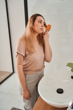 Yapay bacaklı, beyaz bir kadın saçlarını tararken aynaya bakıyor.