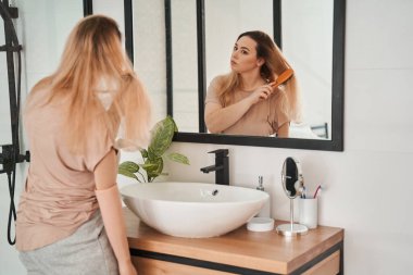 Protez kollu kendine güvenen genç bir kadın yansımasına bakıyor.