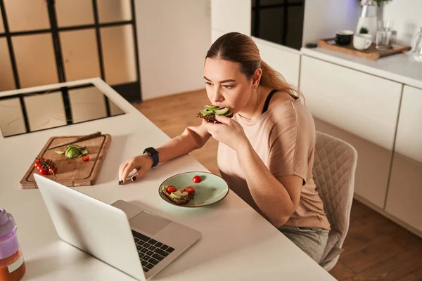 Protez kollu güzel genç bir kadın modern mutfakta yemeğini yiyor.