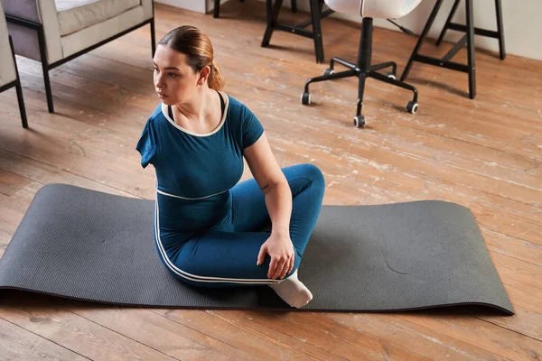 Athletic young woman with amputee arm doing morning exercises at yoga mat