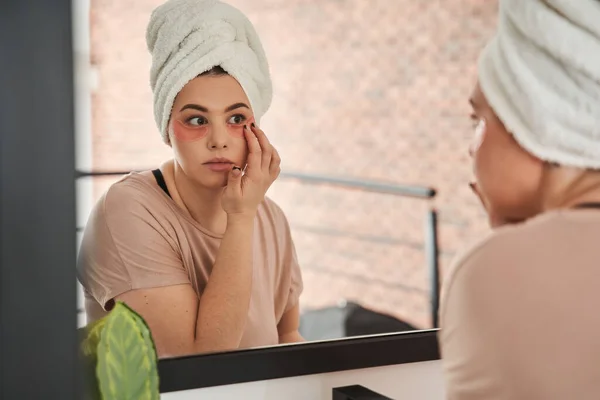 Female is looking into the mirror while wearing eye patches against wrinkles — Stock Photo, Image