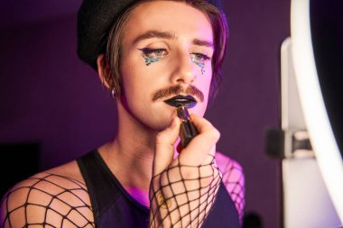 Blogcu adam akıllı telefonun önünde duruyor ve nasıl makyaj yaptığını kaydediyor.