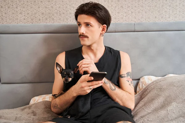Homme sérieux avec une moustache tenant un téléphone portable et regardant ailleurs tout en étant assis — Photo