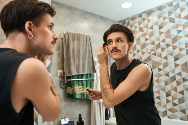Man met een heldere gezonde huid, met wenkbrauwgel op zijn wenkbrauwen en kijkend in de spiegel — Stockfoto