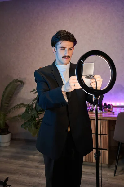 Şık takım elbiseli beyaz adam lambanın önünde duruyor ve akıllı telefonunu ayarlıyor. — Stok fotoğraf