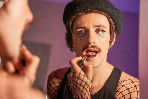 Hombre con bigotes haciendo maquillaje delante del espejo grande mientras se prepara para la fiesta — Foto de Stock