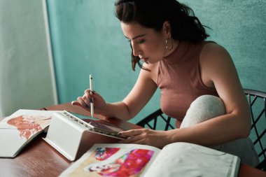 Kafkasyalı yaratıcı kadın çizer masada oturuyor ve tablete çizimler yapıyor.