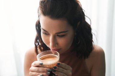 Kumral, kıvırcık saçlı, güzel, mutlu bir kadın. Mutfakta sabah kahvesinin tadını çıkarıyor.