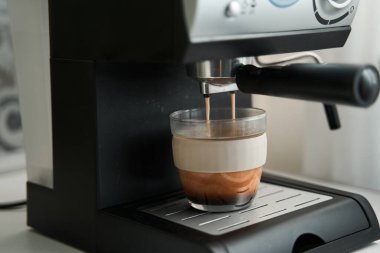 Şeffaf fincan kahve makinesinin ızgarasında duruyor. Restorandaki fincana kahve dökülüyor.