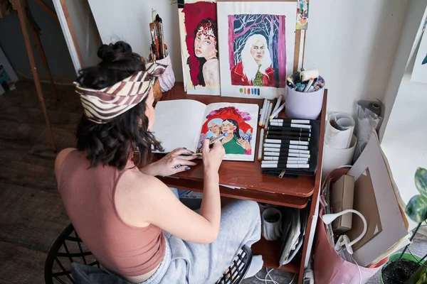 Žena umělec sedí u stolu hůlka dělat nějaké ilustrace s barevnými trhy doma — Stock fotografie