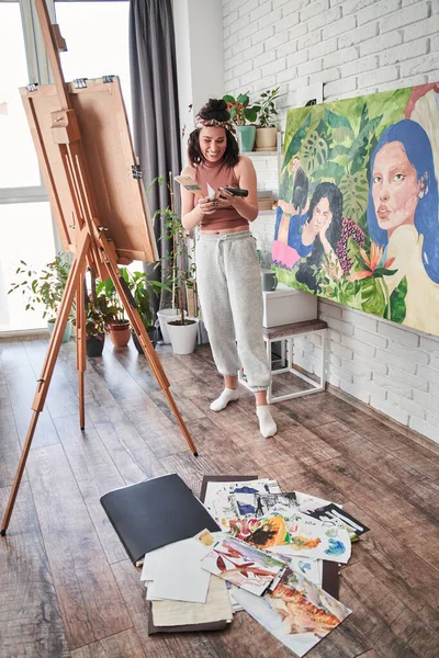 Mujer sosteniendo tubos con pinturas acrílicas mientras se prepara para dibujar cuadros en el caballete en el estudio de arte —  Fotos de Stock