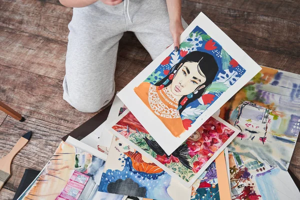 Pintora feminina olhando para seus desenhos enquanto sentada no chão durante o fim de semana — Fotografia de Stock