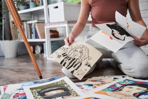 Pintora mirando sus dibujos mientras está sentada en el suelo durante el fin de semana —  Fotos de Stock