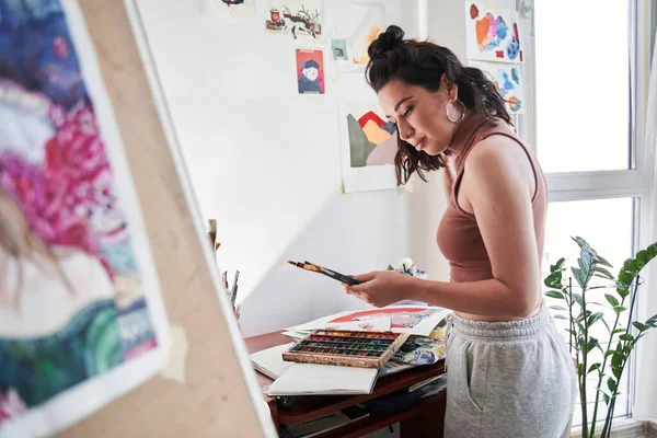 Mulher artista olhando para seus pincéis com cara de prazer enquanto se prepara para o desenho em casa — Fotografia de Stock