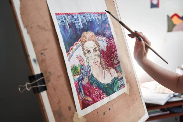 Žena umělec stojí vedle stojanu a drží štětec a umělec paleta, zatímco kreslí své mistrovské dílo — Stock fotografie