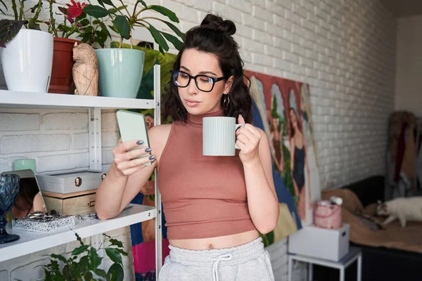 Ηρεμία καυκάσιος καλλιτέχνης γυναίκα πίνοντας καφέ και κοιτάζοντας το smartphone, ενώ έχοντας διάλειμμα — Φωτογραφία Αρχείου
