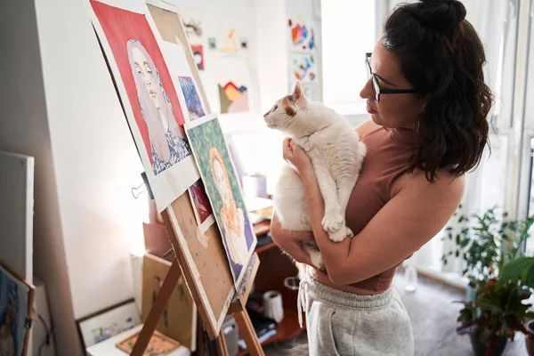 Mulher segurando seu gato doméstico branco nas mãos enquanto estava com ele na frente do cavalete — Fotografia de Stock