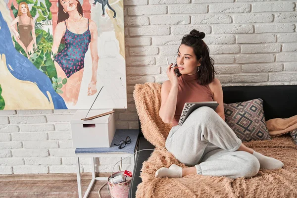 Nő művész ül a kanapén táblagéppel a kezében, és nézi el, miközben gondolkodás új művészeti munka — Stock Fotó