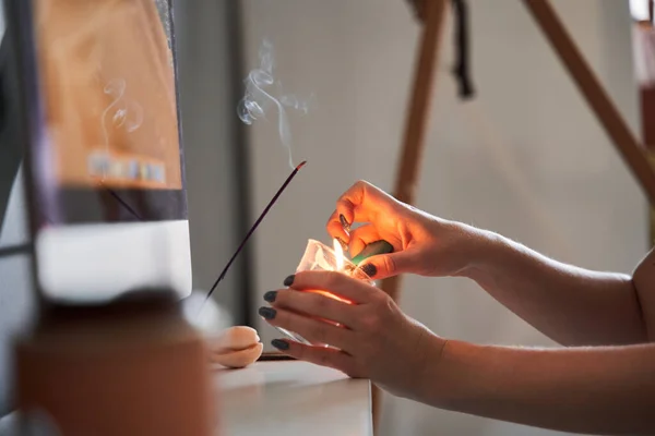 Donna irriconoscibile bruciare aroma bastone e candela mentre si prepara atmosfera accogliente a casa — Foto Stock