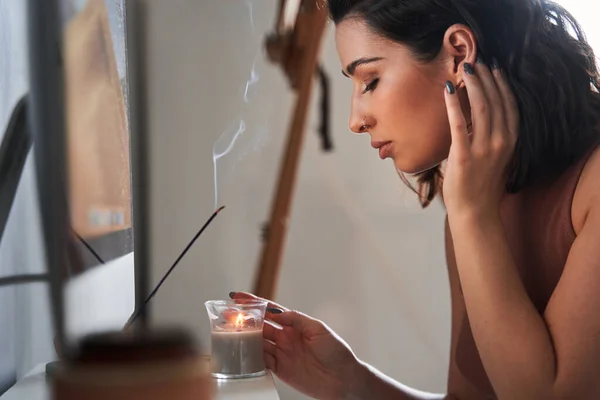 Mujer inhalando aroma de la varilla de aroma y tocando la vela con la mano — Foto de Stock