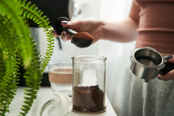 Mulher segurando colher com café e colocá-lo no frasco enquanto prepara a bebida quente da manhã — Fotografia de Stock