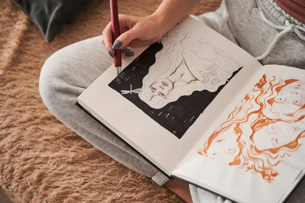 Uvolněná umělkyně sedící u pohovky a kreslící náčrtky na svém zápisníku doma — Stock fotografie