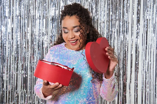 Optimistische multirassische Dame in modischer Festtagskleidung beim Blick auf die Geschenkbox — Stockfoto