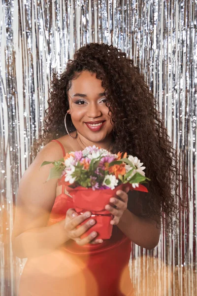 Mädchen mit Blumenstrauß in ihren Händen gratuliert jemandem über silbernen Lametta-Vorhang Hintergrund — Stockfoto
