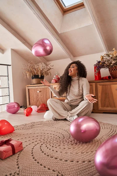 Женщина в домашней одежде сидит на полу в окружении воздушных шаров и веселится — стоковое фото