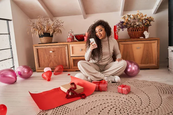 スマートフォンを持っている女性とスタイリッシュな赤い紙に包装した後、彼女のプレゼントを撮影 — ストック写真