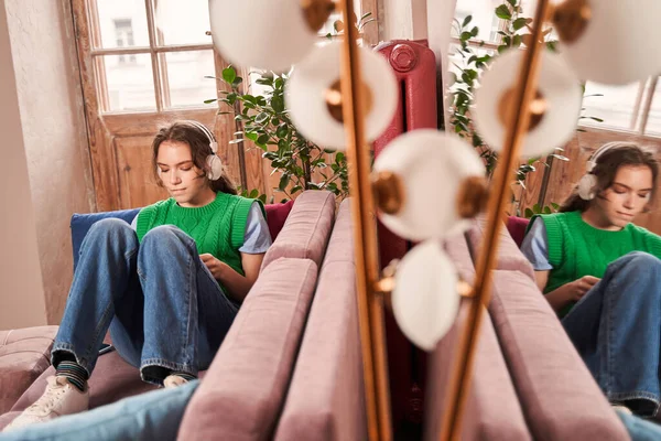Egy tinédzser lány fülhallgatóban hallgatja a kedvenc dalait, miközben a kanapén ül. — Stock Fotó