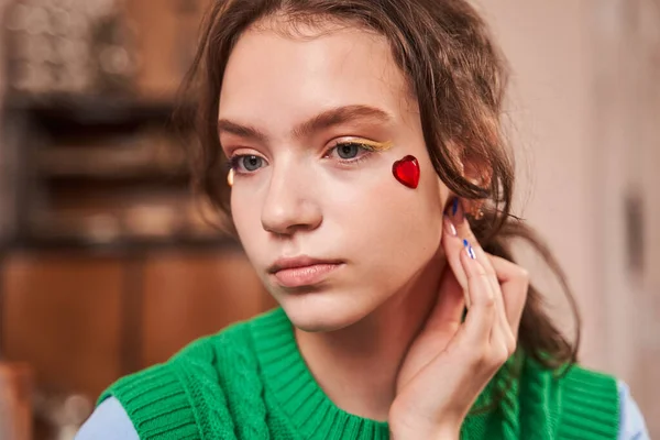 Tiener meisje met helder make-up en strass in hart vorm onderzoeken zichzelf — Stockfoto