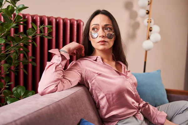 Kaukasiska kvinna med ögonlappar koppla av och titta bort medan du sitter på soffan — Stockfoto