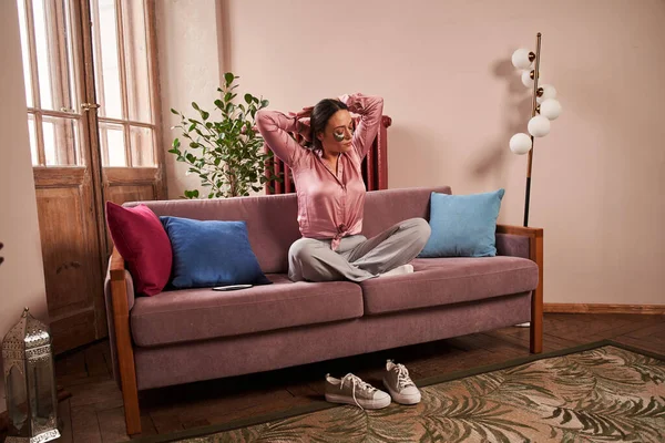 Женщина, сидящая на диване и отдыхающая в позе лотоса, выполняя домашнюю процедуру красоты — стоковое фото