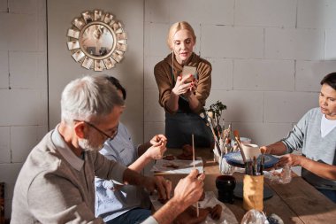Öğretmen, yüksek lisans sınıfında öğrencilerinin akıllı telefonunda fotoğraf çekiyor.