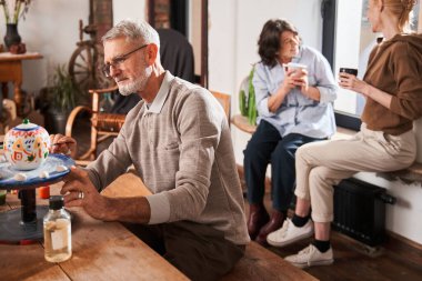 Kıdemli adam masada oturuyor ve el yapımı çaydanlığa kendi çizimlerini yapıyor.