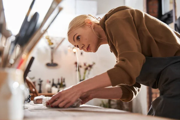 Femme préparant son lieu de travail tout en mettant un morceau d'argile à la table avec un visage concentré — Photo