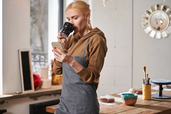 Woman drinking coffee and looking at her smartphone while relaxing after work — Stock fotografie