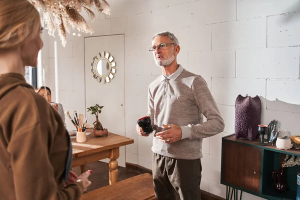 Senior bearded man holding cup and talking something to his young teacher — Stock fotografie