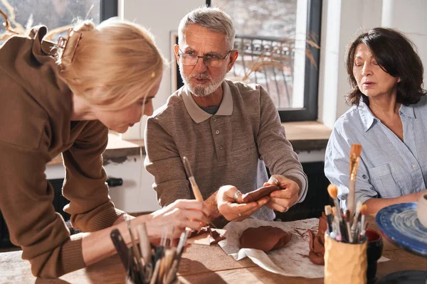 Grey haired bearded man asking his teacher while spending time at the pottery workshop — Stock Photo, Image