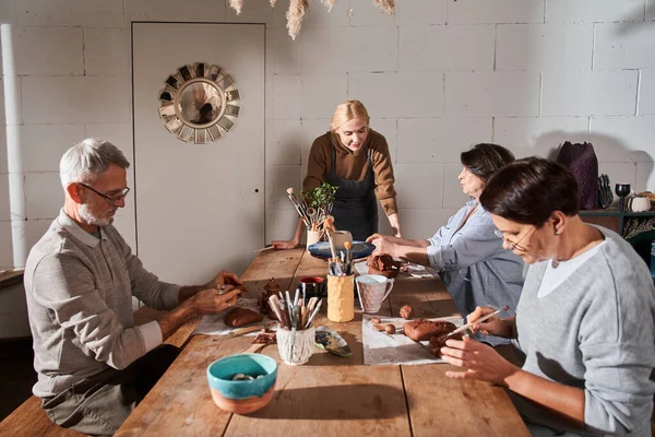 Önlük giyen kadın sanatçı öğrencilerine dikkatle bakıyor.