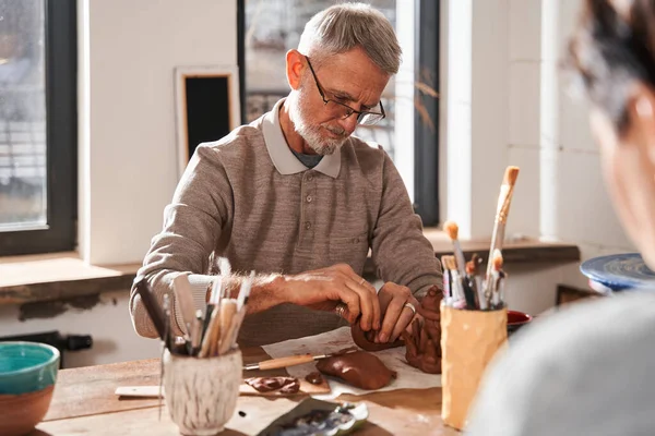 Senior homem atentamente esculpir pratos diferentes da argila na oficina de cerâmica — Fotografia de Stock