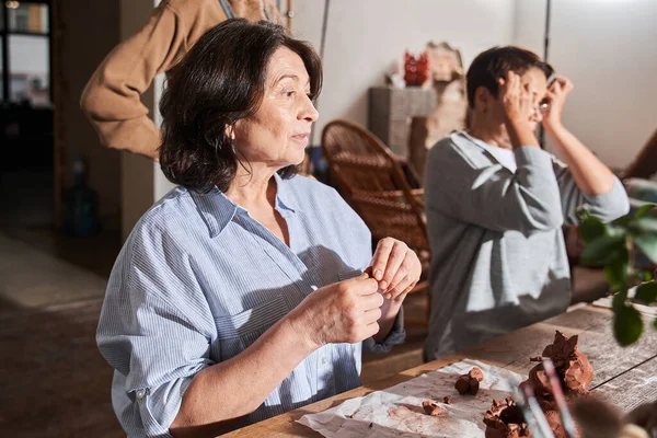 Mujer mayor haciendo platos de arcilla mientras está sentada a la mesa en el taller — Foto de Stock