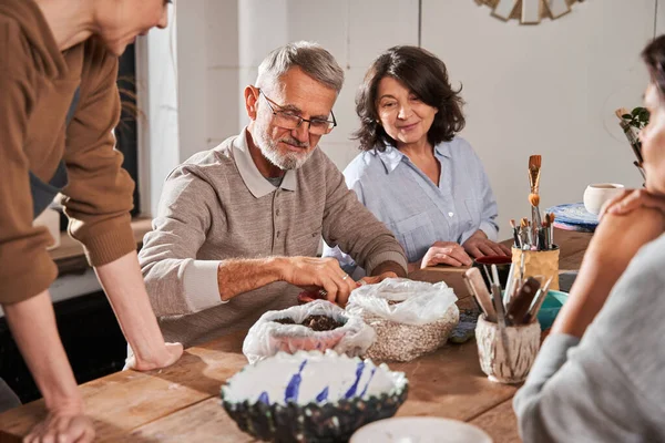 Hombre barbudo mayor sonriendo felizmente y mirando los platos mientras hace platos — Foto de Stock