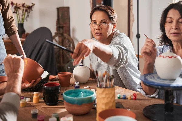 Woman giving brush to her friend while glazing clay pots at the master class — Foto de Stock