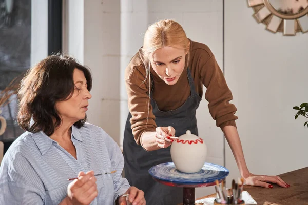 Çömlekçilik yüksek sınıfında çalışırken son sınıf öğrencisine tavsiye veren yetenekli bir tasarımcı.