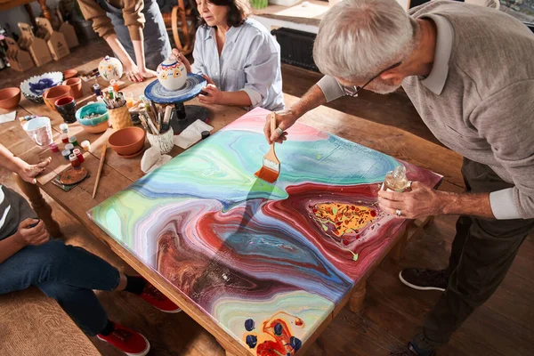 Hombre mayor mirando su pintura abstracta fresca mientras dibuja —  Fotos de Stock